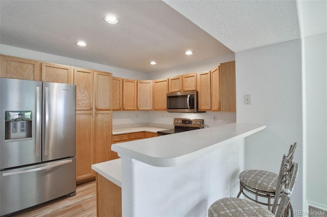 kitchen with light wood-type flooring, light brown cabinets, stainless steel appliances, kitchen peninsula, and a kitchen bar