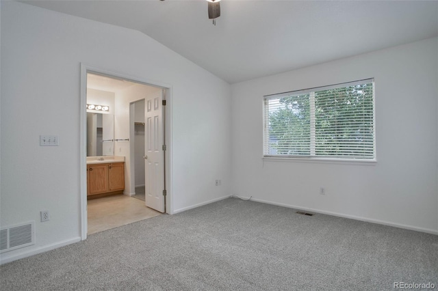 unfurnished bedroom featuring ceiling fan, lofted ceiling, ensuite bath, and light carpet