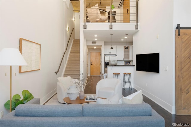 living room featuring wood-type flooring, a barn door, and a high ceiling