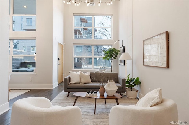 living room with an inviting chandelier, dark wood-type flooring, a healthy amount of sunlight, and a high ceiling