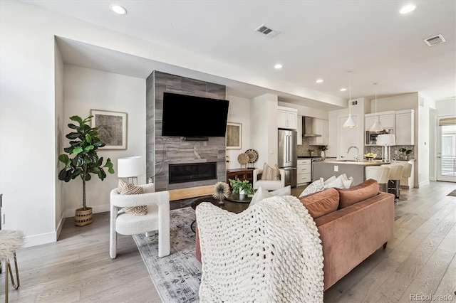 living room with light wood-type flooring, a high end fireplace, and sink