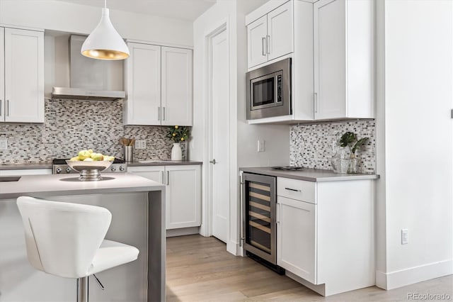 kitchen with pendant lighting, white cabinetry, wall chimney range hood, wine cooler, and stainless steel microwave