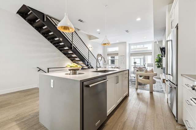 kitchen with white cabinetry, stainless steel appliances, sink, hanging light fixtures, and a kitchen island with sink