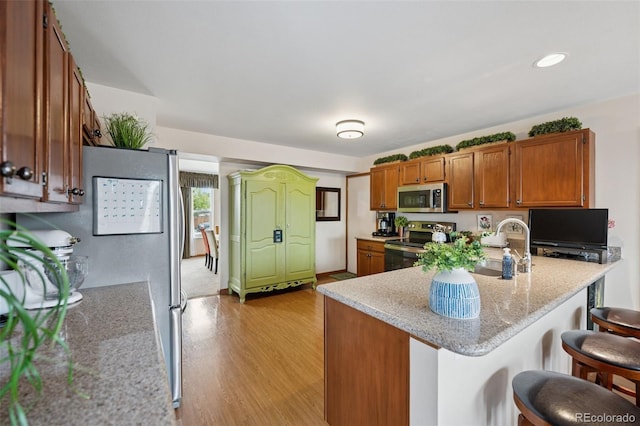 1055 Lindstrom Dr, Colorado Springs, CO 80911 - kitchen featuring appliances with stainless steel finishes, brown cabinetry, a kitchen bar, a peninsula, and light wood finished floors