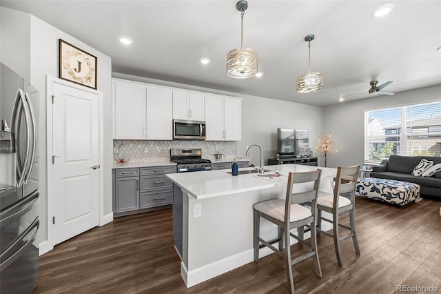 kitchen with appliances with stainless steel finishes, open floor plan, dark wood-style flooring, a sink, and tasteful backsplash