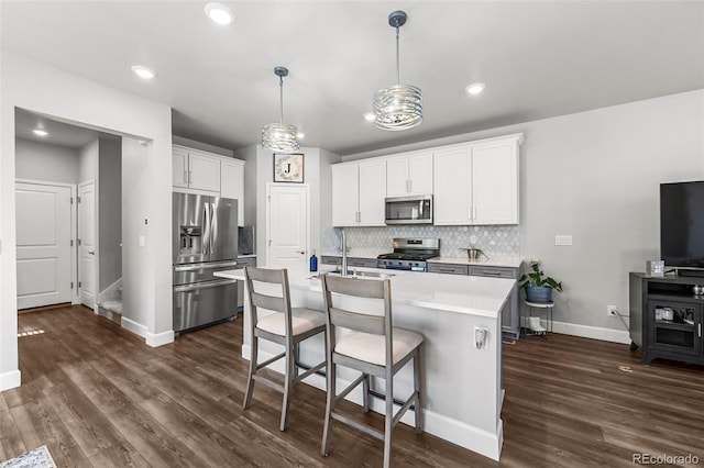 kitchen with stainless steel appliances, a sink, backsplash, dark wood-style flooring, and baseboards