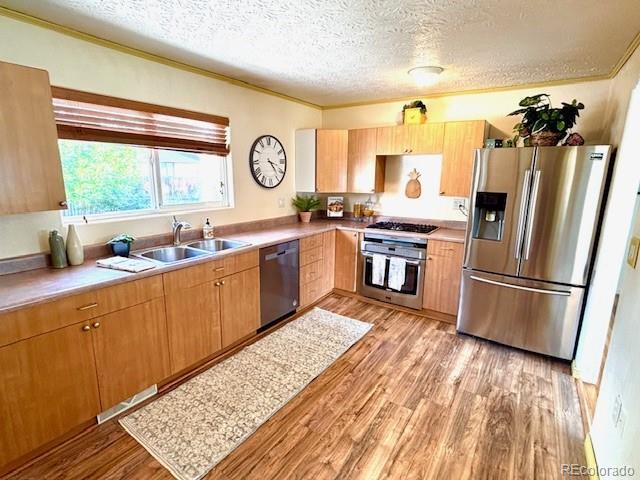 3531 E 91st Ave, Thornton, CO 80229 - kitchen with appliances with stainless steel finishes, a sink, light wood-style flooring, a textured ceiling, and ornamental molding