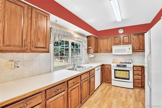 kitchen with white appliances, brown cabinetry, and a sink