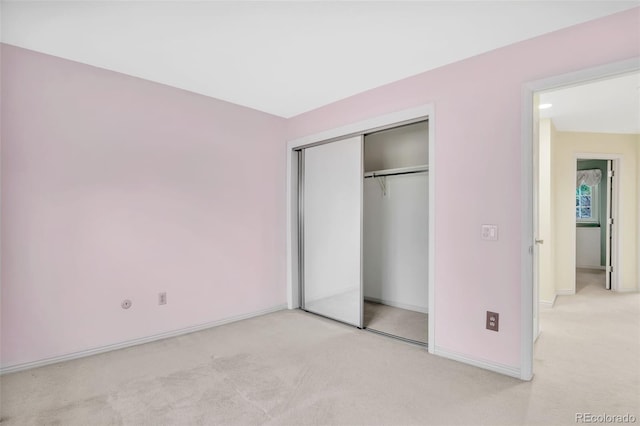 unfurnished bedroom with light carpet, a closet, and baseboards