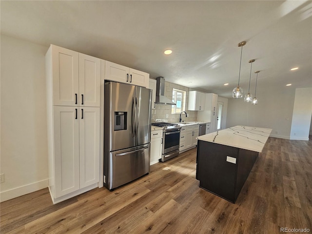 kitchen with white cabinets, a kitchen island, appliances with stainless steel finishes, pendant lighting, and wall chimney exhaust hood