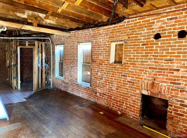 unfurnished living room featuring wood-type flooring, beamed ceiling, and brick wall