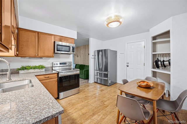 kitchen featuring sink, stainless steel appliances, light stone countertops, and light wood-type flooring