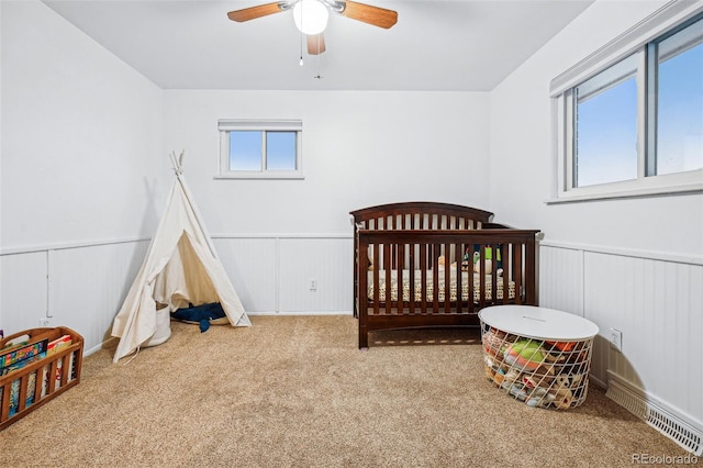 carpeted bedroom with a nursery area and ceiling fan