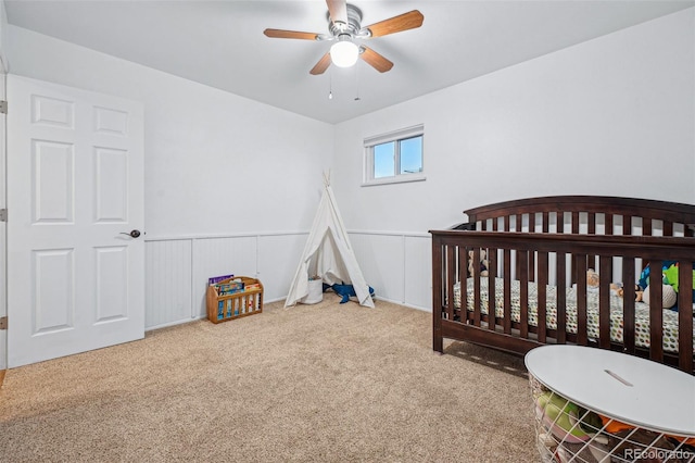 carpeted bedroom with a crib and ceiling fan