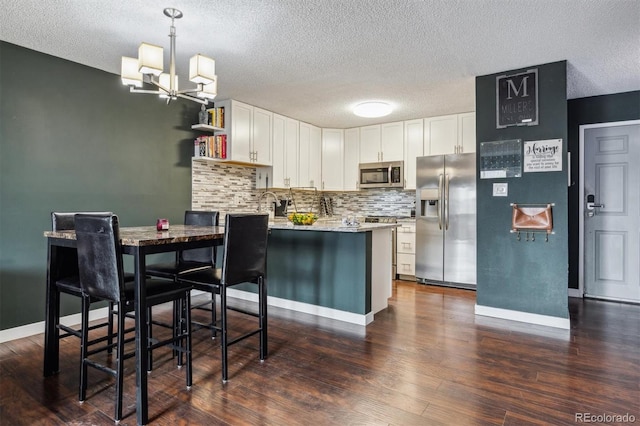 kitchen with kitchen peninsula, dark hardwood / wood-style flooring, appliances with stainless steel finishes, white cabinetry, and decorative light fixtures