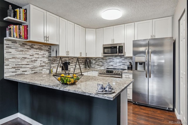 kitchen with light stone countertops, dark hardwood / wood-style flooring, kitchen peninsula, white cabinetry, and stainless steel appliances