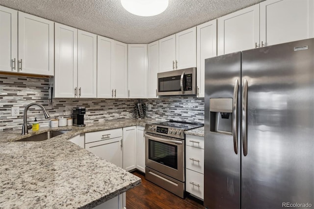 kitchen with dark wood-type flooring, sink, light stone countertops, white cabinets, and appliances with stainless steel finishes