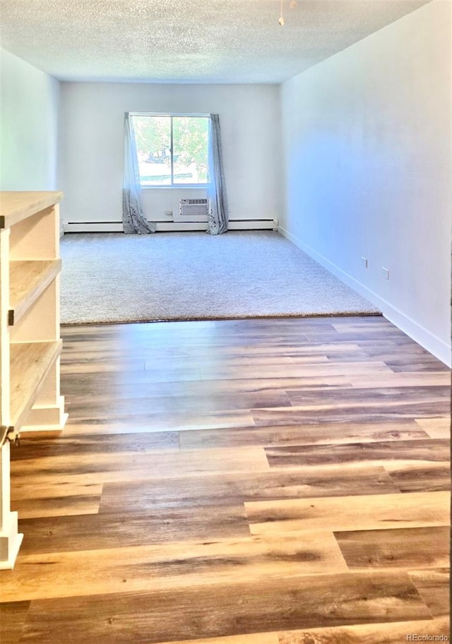 unfurnished room featuring hardwood / wood-style flooring, a baseboard heating unit, and a textured ceiling