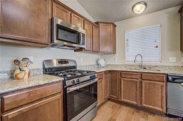 6812 Indian Paintbrush St, Frederick, CO 80530 - kitchen with appliances with stainless steel finishes, a sink, light wood-style flooring, light stone counters, and brown cabinets
