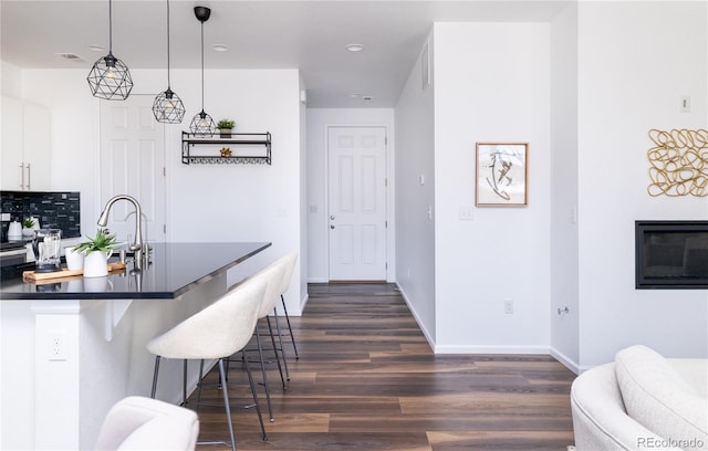 kitchen with dark hardwood / wood-style floors, decorative light fixtures, white cabinets, a kitchen bar, and decorative backsplash