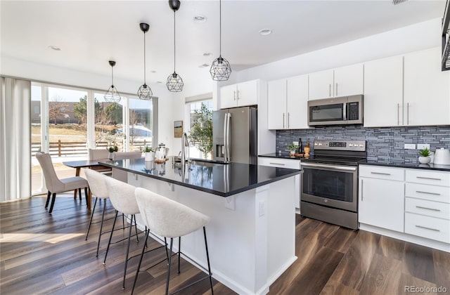 kitchen featuring decorative light fixtures, white cabinetry, an island with sink, sink, and stainless steel appliances