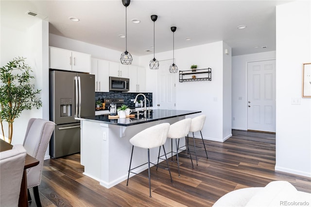 kitchen with a kitchen bar, white cabinetry, tasteful backsplash, appliances with stainless steel finishes, and pendant lighting