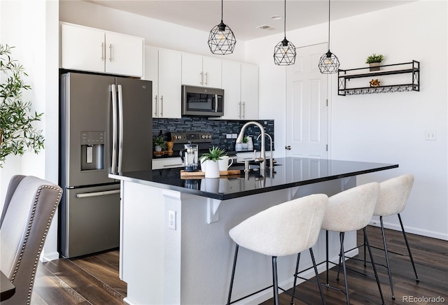 kitchen featuring decorative light fixtures, tasteful backsplash, white cabinetry, stainless steel appliances, and a center island with sink