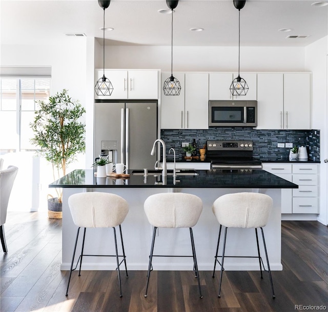 kitchen with appliances with stainless steel finishes, a kitchen island with sink, hanging light fixtures, and white cabinets