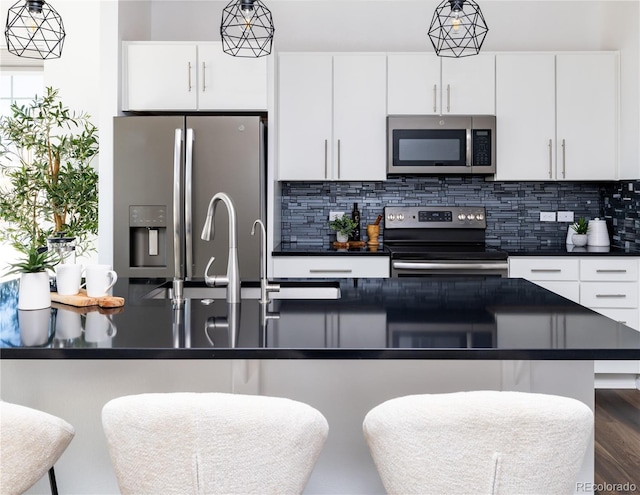 kitchen featuring stainless steel appliances, white cabinetry, a kitchen breakfast bar, and decorative light fixtures