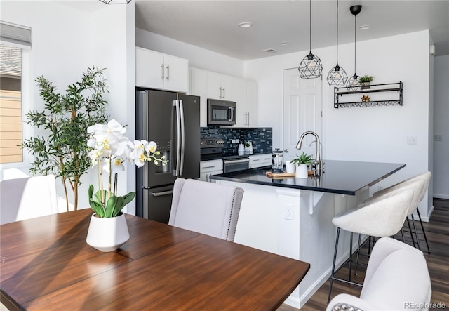 kitchen with a breakfast bar area, decorative light fixtures, white cabinets, stainless steel appliances, and backsplash