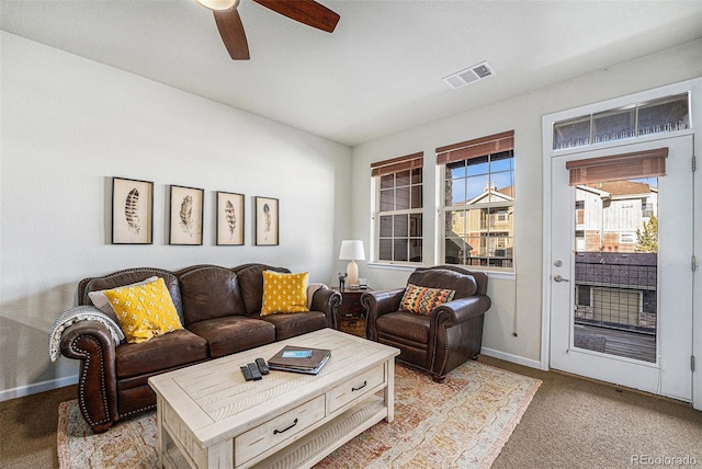 living area featuring baseboards, visible vents, ceiling fan, and light colored carpet