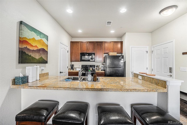 kitchen featuring a breakfast bar area, a peninsula, a sink, visible vents, and black appliances