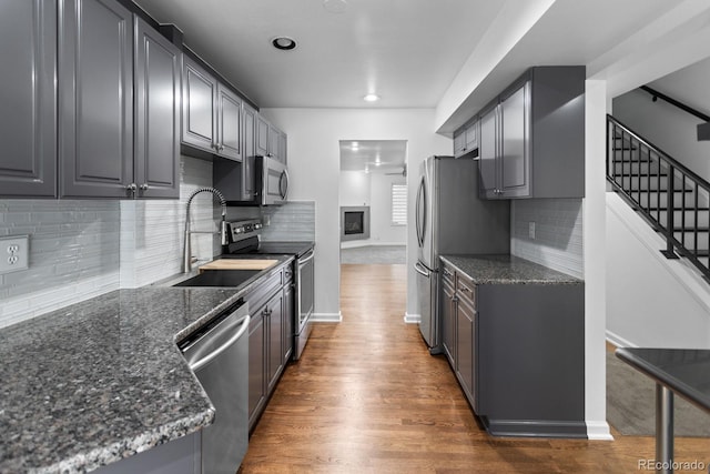 kitchen with appliances with stainless steel finishes, tasteful backsplash, sink, dark stone counters, and dark wood-type flooring