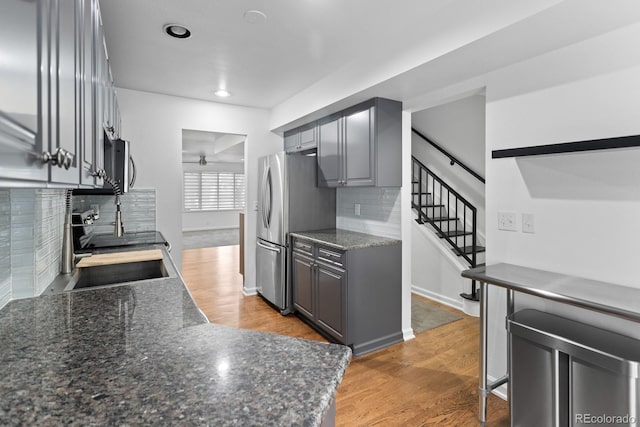 kitchen with tasteful backsplash, light wood-type flooring, appliances with stainless steel finishes, ceiling fan, and dark stone counters