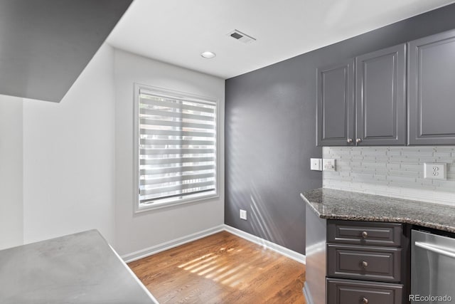 kitchen featuring a healthy amount of sunlight, dark stone counters, hardwood / wood-style floors, and decorative backsplash