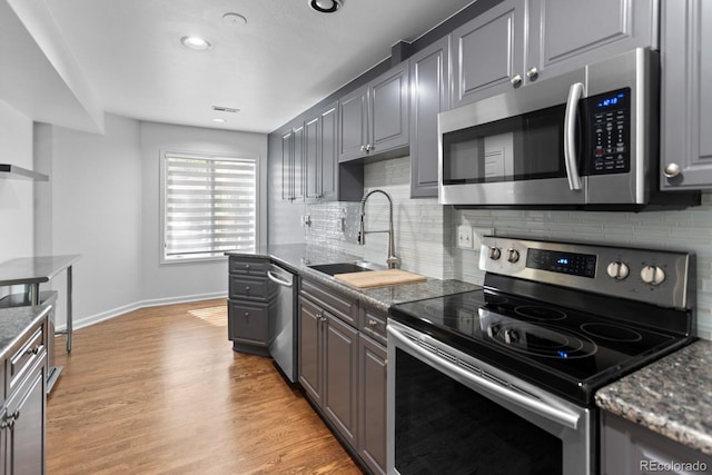 kitchen with appliances with stainless steel finishes, sink, light wood-type flooring, and decorative backsplash