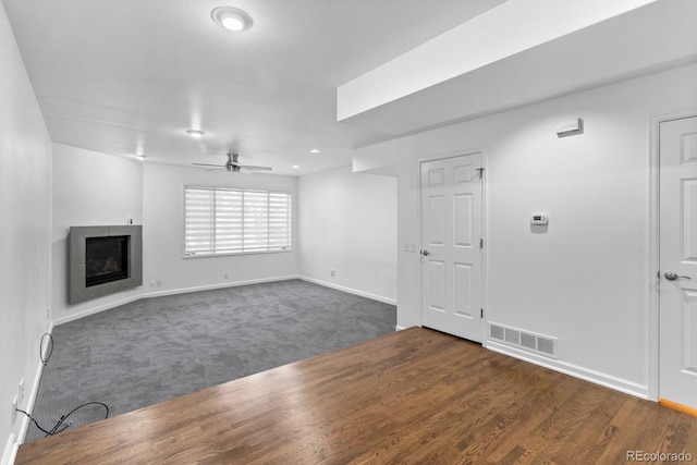 unfurnished living room featuring a tiled fireplace, dark carpet, and ceiling fan