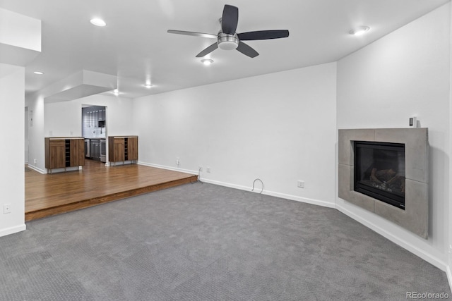 unfurnished living room with ceiling fan, carpet floors, and a tile fireplace