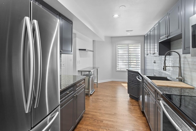 kitchen featuring sink, dark stone countertops, hardwood / wood-style flooring, stainless steel appliances, and backsplash