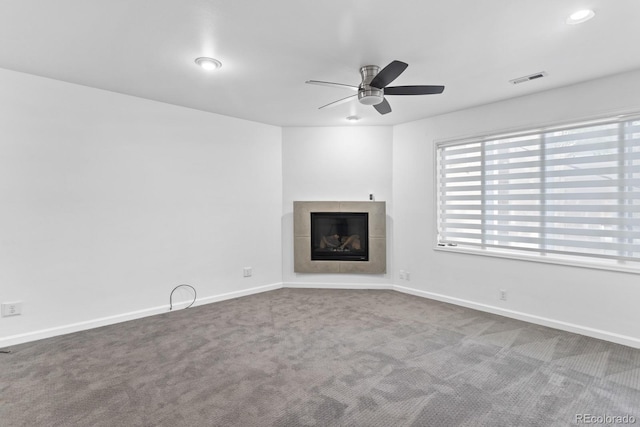 unfurnished living room with a tile fireplace, carpet, and ceiling fan