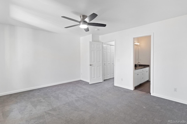 unfurnished bedroom with sink, ensuite bath, dark carpet, a closet, and ceiling fan