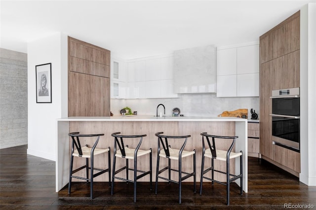 kitchen featuring dark wood-type flooring, modern cabinets, a breakfast bar, and double oven