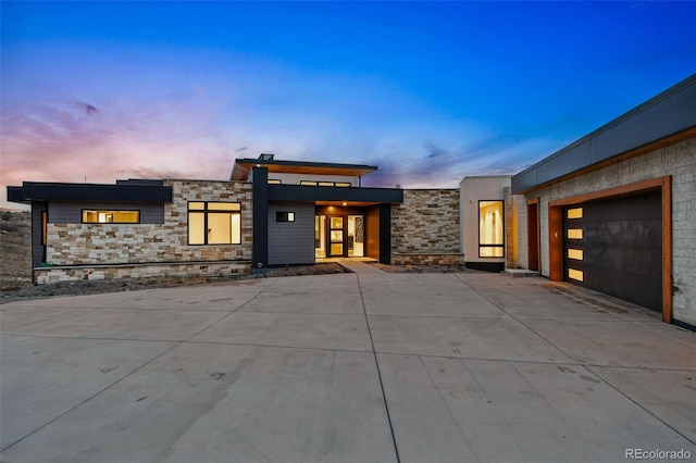 contemporary house with stone siding, a garage, and concrete driveway
