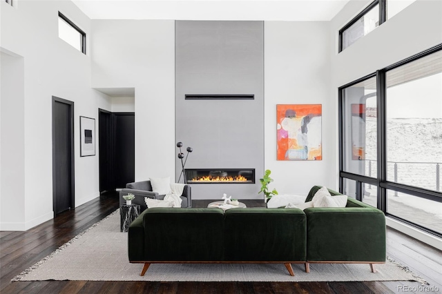 living area with hardwood / wood-style floors, baseboards, a towering ceiling, and a glass covered fireplace