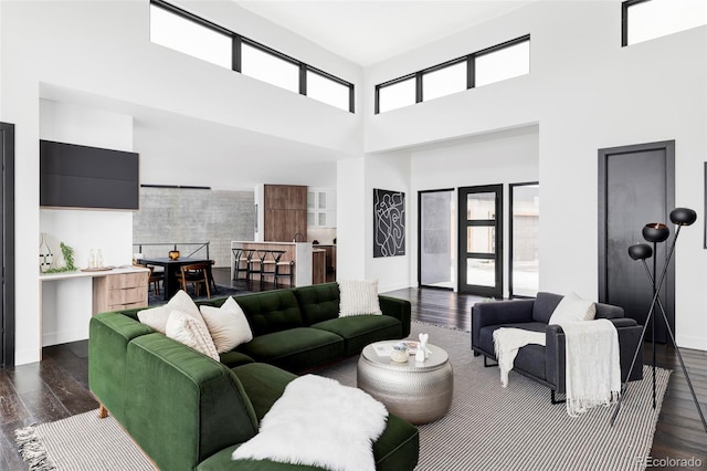living room with dark wood-type flooring, a towering ceiling, and baseboards