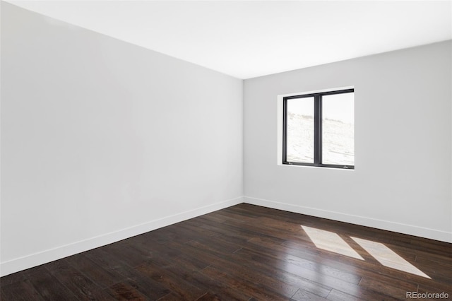 spare room featuring baseboards and dark wood-type flooring