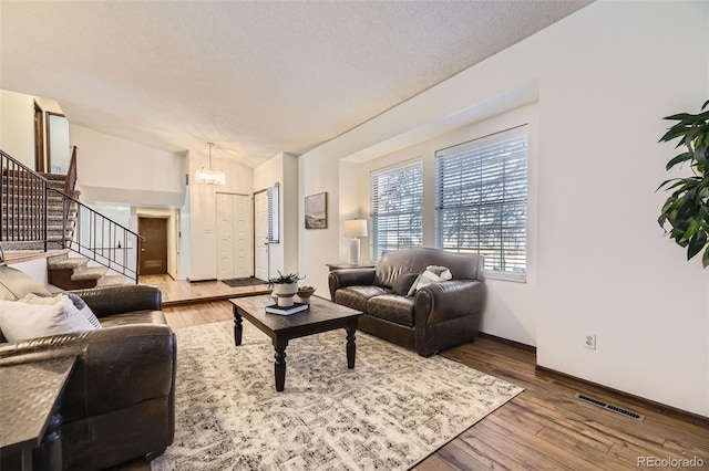 living room featuring hardwood / wood-style flooring, stairs, baseboards, visible vents, and a notable chandelier