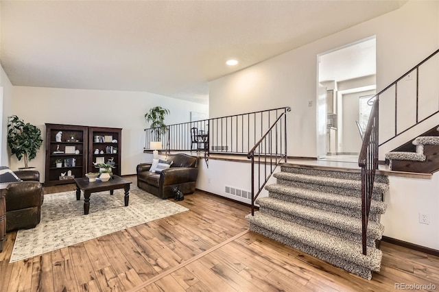 living room with stairs, visible vents, baseboards, lofted ceiling, and hardwood / wood-style flooring