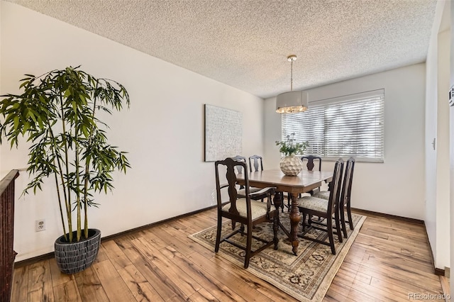 dining space featuring an inviting chandelier, a textured ceiling, baseboards, and light wood-type flooring