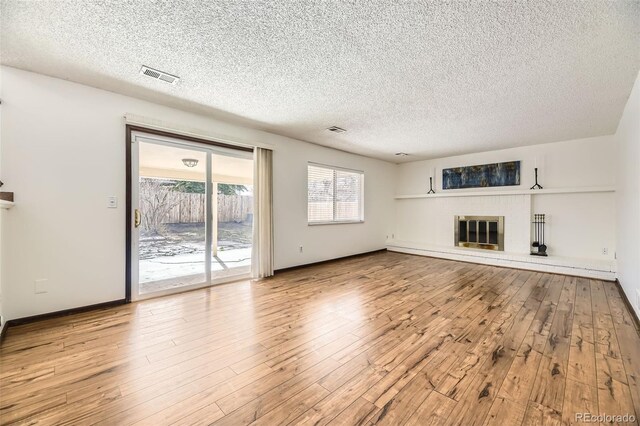 unfurnished living room featuring a textured ceiling, a brick fireplace, wood-type flooring, and visible vents